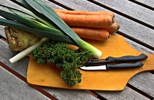 Suppengrün mit Schäler, Gemüsemesser und Schneidebrett - Grundlage für eine gesunde Hühnersuppe